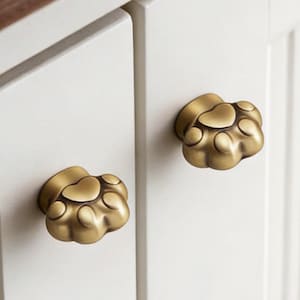 May include: A white cabinet with two brass paw-shaped knobs. The knobs are a warm gold colour and are fixed to the white cabinet doors. The cabinet has a dark brown wooden top. The cabinet doors have vertical grooves.