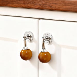 以下が含まれることがあります： 磨かれたクロム仕上げと木製の球形ハンドルを備えた2つのキャビネットプル。プルは白いキャビネットドアに取り付けられています。木製のハンドルは、暖かく、ミディアムブラウンの色です。