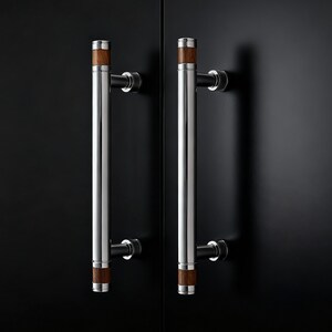 May include: Two stainless steel door handles with wooden accents. The handles are cylindrical with a polished finish and are mounted on a black surface. The wooden accents are at the top and bottom of the handles.