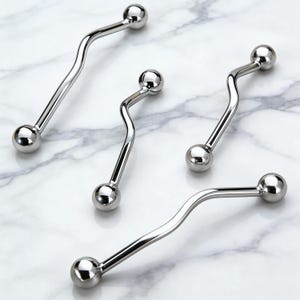 Könnte beinhalten: Vier glänzende, silberfarbene Barbell-Piercings mit geschwungenem, wellenförmigem Design. Jedes Barbell hat an jedem Ende eine kleine, runde Kugel. Die Piercings sind auf einer weißen Marmoroberfläche angeordnet.