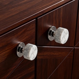 Może przedstawiać: Zbliżenie na ciemnobrązową drewnianą szafkę z dwoma marmurowymi i chromowanymi gałkami. Gałki są cylindryczne z białym i szarym wzorem marmuru. Szafka ma geometryczny wzór.