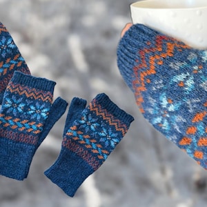 Könnte beinhalten: Blaue Strick-Fingerhandschuhe und Fäustlinge mit einem Schneeflocken- und geometrischen Muster in Orange, Hellblau und Lila. Eine Hand hält eine weiße Tasse. Die Handschuhe und Fäustlinge werden vor einem verschwommenen, schneebedeckten Hintergrund gezeigt.
