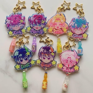 Könnte beinhalten: Eine Sammlung von Schlüsselanhängern mit Anime-Charakteren. Jeder Schlüsselanhänger zeigt ein farbenfrohes Charakterdesign mit einem sternförmigen Anhänger und einer Miniatur-Limonadenflasche. Die Charaktere haben unterschiedliche Haarfarben und sind mit Namen versehen.