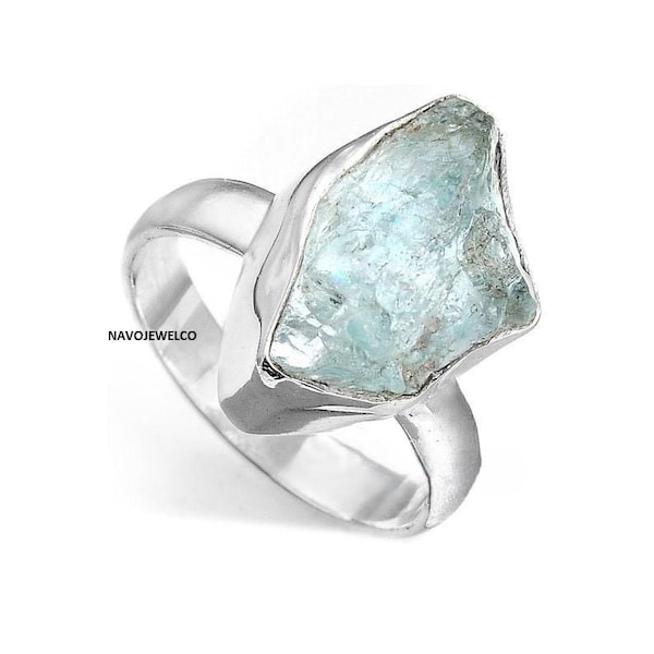 May include: A silver ring featuring a large, irregular-shaped, pale blue gemstone. The ring has a simple, polished band and a bezel setting that highlights the natural form of the stone. The ring is set against a white background.