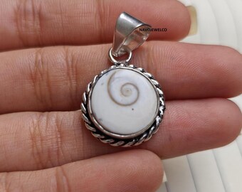 May include: A circular pendant featuring a white shiva eye shell with a natural brown spiral pattern, set in a twisted silver metal frame with a smooth silver bail at the top. The text NAVOJEWELCO is visible on the silver bail of the pendant.