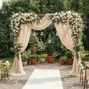 May include: An outdoor wedding ceremony setup featuring a wooden arch draped with cream-colored fabric and adorned with white flowers and greenery. A white aisle runner leads to the arch, with chairs and potted plants on either side.