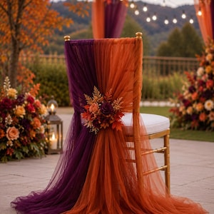 Può includere: Una sedia color oro drappeggiata con tessuto di tulle trasparente viola e arancione bruciato. Lo schienale della sedia è decorato con una composizione floreale centrale composta da fiori dai colori autunnali, foglie secche e fogliame nei toni del rosso, arancione e viola intenso.
