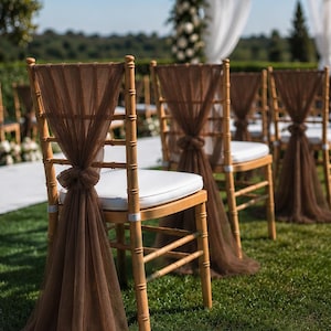 May include: A light wood Chiavari chair featuring a white seat cushion and a sheer brown tulle sash draped over the backrest, tied in a knot at the center. The fabric extends downward to the ground, creating a decorative accent for the chair.