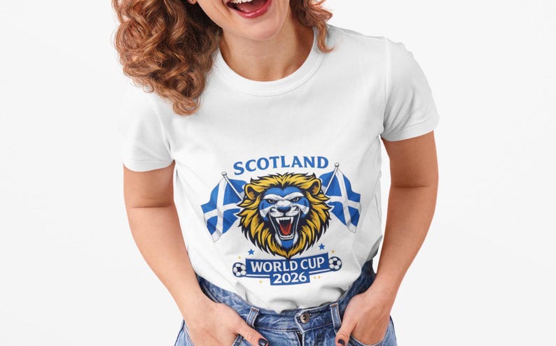 May include: White t-shirt featuring a lion graphic with the text "SCOTLAND WORLD CUP 2026". The lion has a blue and yellow design, with two Scottish flags on either side. The shirt is a crew neck style.