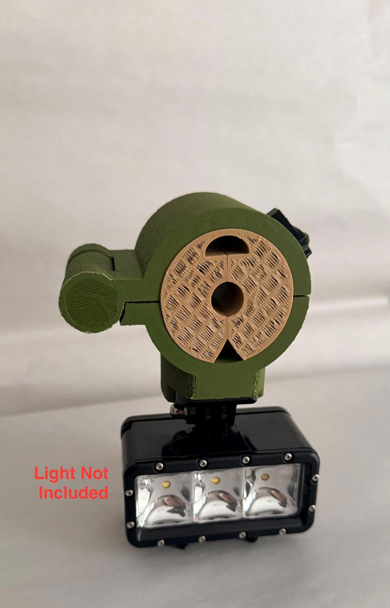 May include: A black and green headlamp mount with a light fixture. The mount is olive green with a tan-colored circular piece. The light fixture has three bright lights. Text on the image reads "Light Not Included."