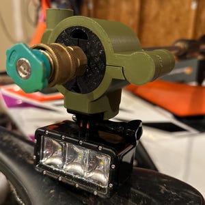 May include: A custom-built device featuring a green and brass nozzle, a black LED light bar, and a green housing. The light bar has three bright LED lights. The device is mounted on a black surface.