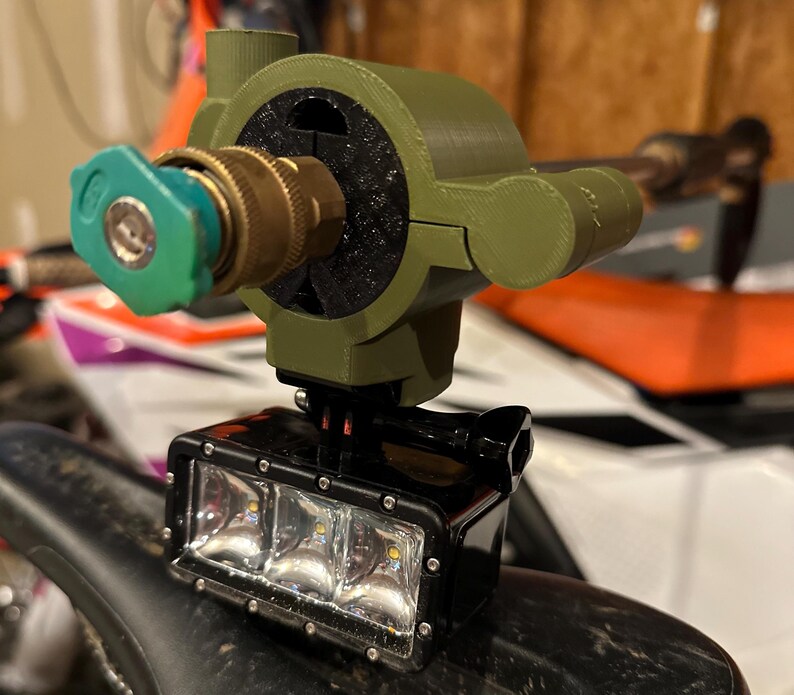 May include: A custom-built device featuring a green and brass nozzle, a black LED light bar, and a green housing. The light bar has three bright LED lights. The device is mounted on a black surface.
