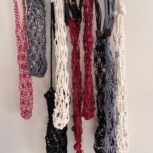 Puede incluir: Una colecci&oacute;n de colgadores de plantas de macram&eacute; en varios colores, incluyendo rojo, gris, negro y blanco. Algunos colgadores presentan detalles de cuero. Los colgadores est&aacute;n dise&ntilde;ados para sostener plantas en macetas y a&ntilde;adir un toque decorativo.