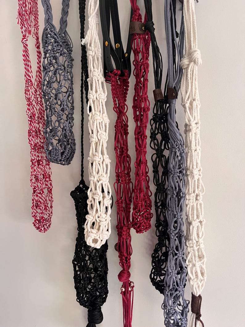 Puede incluir: Una colecci&oacute;n de colgadores de plantas de macram&eacute; en varios colores, incluyendo rojo, gris, negro y blanco. Algunos colgadores presentan detalles de cuero. Los colgadores est&aacute;n dise&ntilde;ados para sostener plantas en macetas y a&ntilde;adir un toque decorativo.