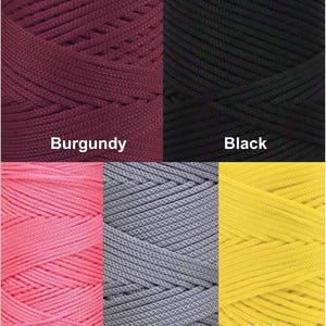 Puede incluir: Primer plano de seis carretes de cord&oacute;n en varios colores. Los colores incluyen burdeos, negro, rosa, gris y amarillo. Cada carrete est&aacute; etiquetado con el nombre de su color. Los cordones parecen estar hechos de un material tejido.
