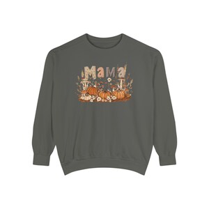 May include: A dark gray long-sleeve sweatshirt featuring a graphic print of the word MAMA in patterned letters, surrounded by orange pumpkins, white flowers, and mushrooms. The design is centered on the chest of the garment.