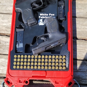 Può includere: Una custodia rigida rosso brillante con un inserto in schiuma nera contenente due pistole semiautomatiche nere, due caricatori neri e quarantotto cartucce con bossolo in ottone. L'inserto riporta la scritta White Fox Fabrication.