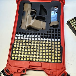 May include: A red, hard-shell case with a black interior, holding a tan and black handgun, a magazine, and numerous bullets. The case is open, revealing the contents. The bullets are arranged in rows, with a mix of gold and silver casings.