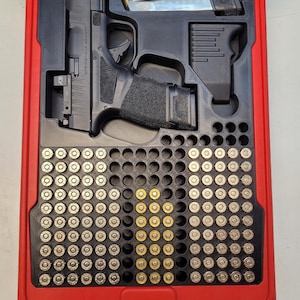 May include: A red case with a black interior, holding a black handgun, a magazine, and numerous bullets. The handgun is marked "SPRINGFIELD ARMORY". The case is designed to securely store and transport firearms and ammunition.