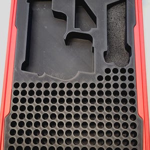 May include: Red and black storage case with a foam insert. The insert has cutouts for various items, including a rectangular section, a triangular section, and a grid of small circular holes. The case is open, revealing the interior.