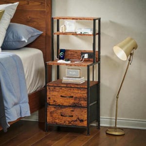 May include: A rustic nightstand with a black metal frame and two drawers. The nightstand has a wooden top and shelves, with a built-in charging station. A gold-colored floor lamp stands beside the nightstand.
