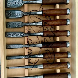 May include: A set of ten chisels with patterned steel blades and dark wooden handles, neatly arranged in a wooden box. The blades have a unique, swirling design. The text "Lord of Metal" is visible on the image.
