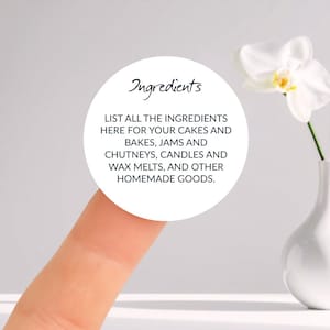 May include: A white circular label with the word "Ingredients" in cursive script. The label includes instructions to list ingredients for cakes, jams, candles, wax melts, and other homemade goods. A white orchid flower is in a white vase.