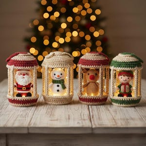 May include: Four crocheted Christmas lanterns with festive characters: Santa Claus, a snowman, a reindeer, and an elf. Each lantern is lit with warm white lights, creating a cozy holiday ambiance. The lanterns are set on a wooden surface.
