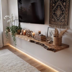 Pode incluir: Uma prateleira de madeira com borda natural com vários itens decorativos. Apresenta velas, livros, uma cesta de vime com plantas secas e obras de arte emolduradas. Uma grande televisão preta está montada acima. A prateleira tem cerca de 183 cm de comprimento.