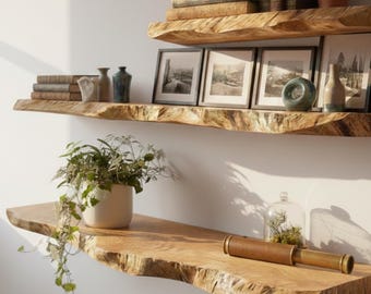 Pode incluir: Duas prateleiras rústicas de madeira montadas numa parede branca. As prateleiras exibem livros, fotos em preto e branco emolduradas, vasos, uma planta em vaso, uma cúpula de vidro decorativa e um telescópio de latão vintage. As prateleiras têm uma borda natural.