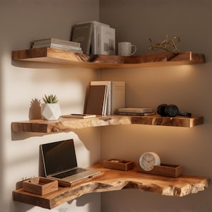 Puede incluir: Tres estanterías de esquina de madera con borde natural, llenas de libros, un portátil, una taza, una planta y otros objetos decorativos. Las estanterías están iluminadas con una cálida iluminación, creando un ambiente acogedor.
