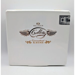 May include: A rectangular white wooden cigar box featuring the brown printed text Villiger Cuellar Connecticut Kreme, along with winged graphics, the phrases Hand Made 1998 and 1998 Long Filler, and a small rectangular warranty seal in the top right corner.