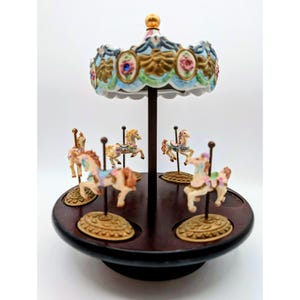 May include: A decorative carousel figurine featuring a dark brown circular wooden base and a central pole supporting a scalloped canopy with floral accents. Four miniature horses in various poses are mounted on individual gold-toned bases.