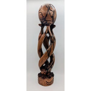 May include: A tall, hand-carved wooden sculpture featuring a smooth, spherical top supported by three intertwined, elongated figures that spiral downward to a circular base. The wood displays a natural brown grain with dark, charred accents.