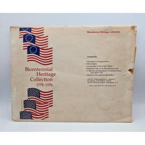 May include: A cream-colored paper folder titled Bicentennial Heritage Collection 1776-1976, featuring illustrations of American flags. The text lists contents including the Declaration of Independence, Bill of Rights, and Constitution of the United States.