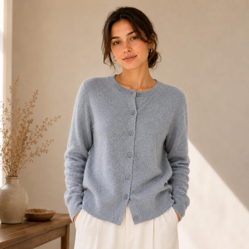 May include: A light blue long-sleeved cardigan with a round neckline and a front button closure. The knit garment features a ribbed hem and cuffs, with matching blue buttons running down the centre placket, providing a simple and clean design.