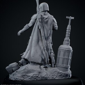 May include: A gray resin render of a Mandalorian figure, posed with a rifle and a cylindrical object. The figure is on a rocky base. The text "23 STL PARTS" is visible.