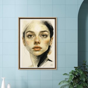 May include: A framed watercolour portrait of a woman with freckles and dark hair. The artwork features a neutral colour palette with shades of beige, brown, and black. The woman's gaze is direct, and the artwork is displayed on a light blue tiled wall.