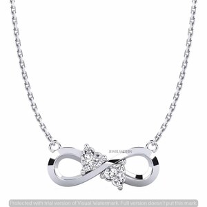 May include: A silver-toned infinity pendant necklace featuring two heart-shaped clear stones set within the center of the infinity symbol. The pendant is attached to a delicate silver-toned chain. The text JEWELSMITHIN is visible on the pendant.