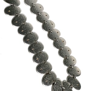 May include: A silver necklace with a textured finish and small gold accents. The necklace is made up of a series of oval-shaped links.