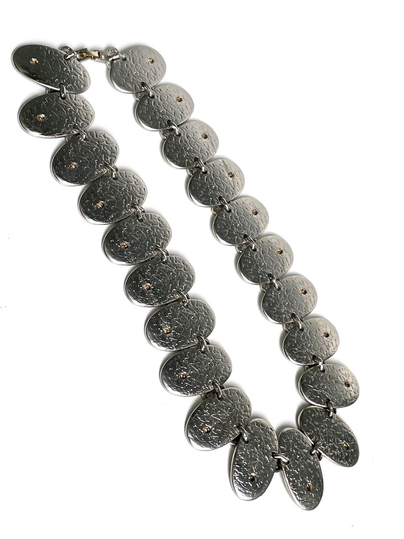May include: A silver necklace with a textured finish and small gold accents. The necklace is made up of a series of oval-shaped links.