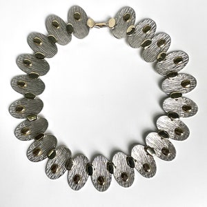 May include: A silver and gold necklace with oval-shaped links. Each link has a textured surface and is accented with small gold dots.