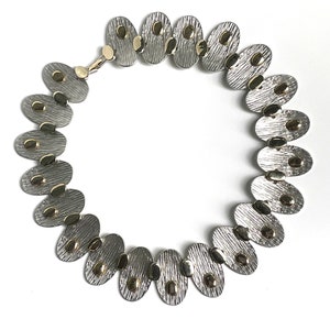 May include: A silver and gold necklace with oval-shaped links. Each link has a textured surface and gold accents.