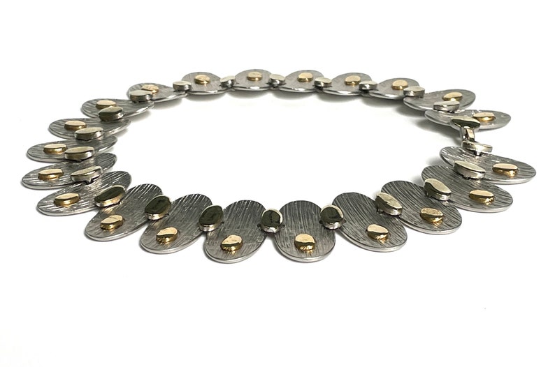 May include: A silver necklace with gold accents. The necklace is made of oval-shaped links with a textured surface. The gold accents are small, round pieces that are attached to the links.