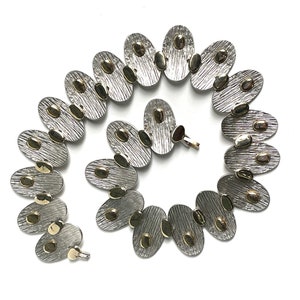 May include: A silver and gold necklace with oval-shaped links. Each link has a textured surface and is decorated with small gold dots.