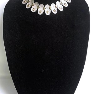May include: A silver necklace with oval-shaped links and gold accents. The necklace is displayed on a black velvet mannequin bust.