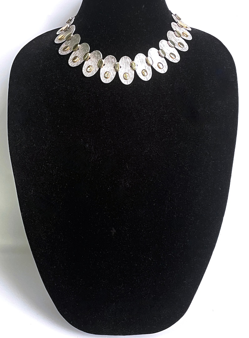 May include: A silver necklace with oval-shaped links and gold accents. The necklace is displayed on a black velvet mannequin bust.