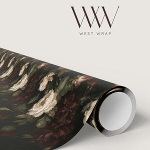 Puede incluir: Un rollo de papel de regalo con fondo negro y un estampado floral de rosas blancas y burdeos oscuro con hojas verdes. El logotipo WW WEST WRAP est&aacute; impreso en color marr&oacute;n oscuro sobre el rollo, en un fondo de color neutro claro.