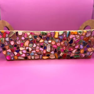 May include: A rectangular decorative tray with a mosaic design. The tray is covered in small, irregularly shaped pieces of colourful stones in shades of pink, purple, green, and yellow. It has two wooden handles.