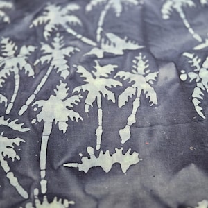 May include: Close-up of a fabric with a repeating pattern of white palm trees against a dark blue background. The fabric has a slightly wrinkled texture, suggesting it may be cotton or linen. The design evokes a tropical or beach theme.